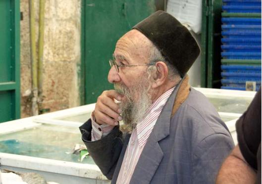 man brown fez in market with hand to mouth standing uncertain and undecided