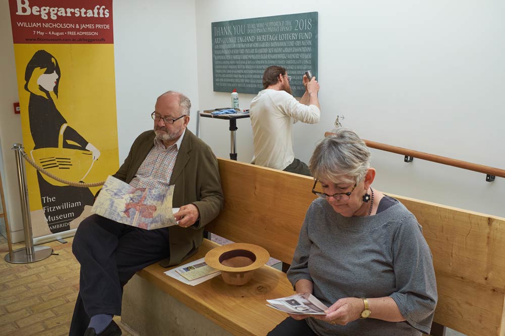 man inscribing a stone plaque with hammer and chisel while others sit and read