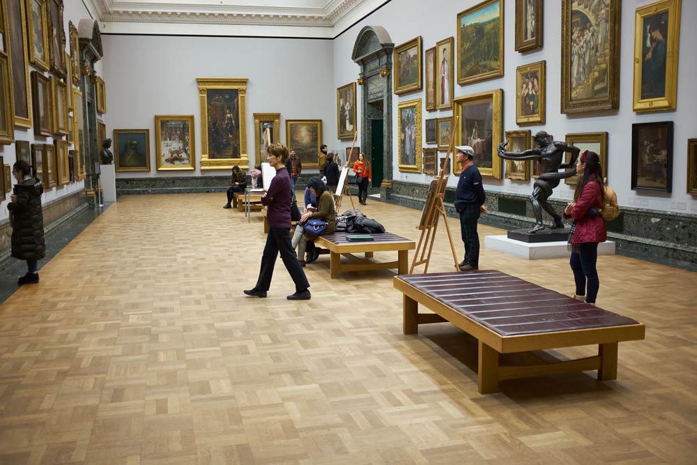 A room of paintings in Tate Britain with sketch easels and people looking at the paintings