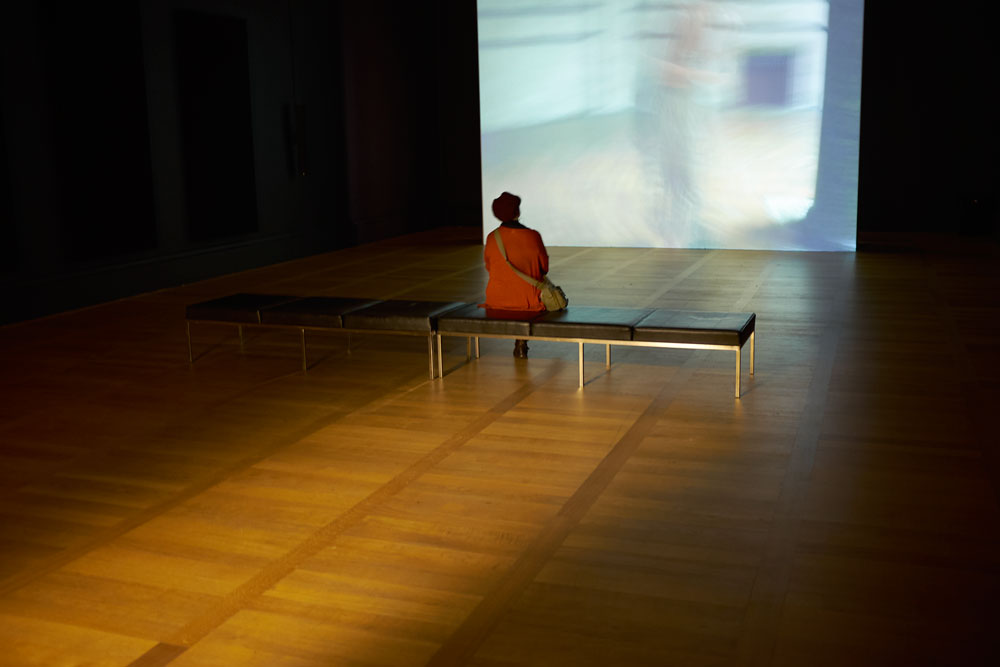 Woman sitting alone in a room in Tate Britain, watching a film in near darkness